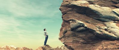 A man stands before a large rock.