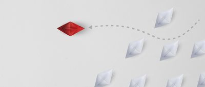 A red paper boat navigates through a group of grey ones.