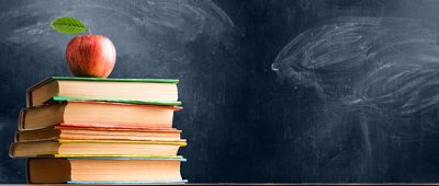 School accessories, books and fresh apple against chalkboard