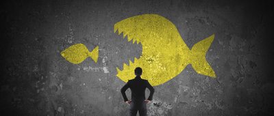 A figure stands before an artwork in which a small fish is about to be eaten by a large fish.