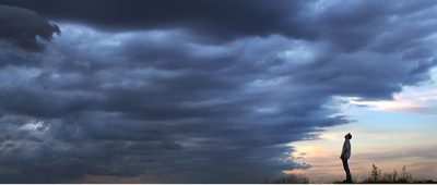 A person stands underneath cloudy skies.