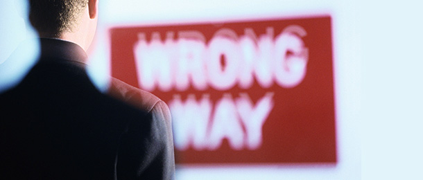 A red and white sign reading wrong way seen over shoulder of a man